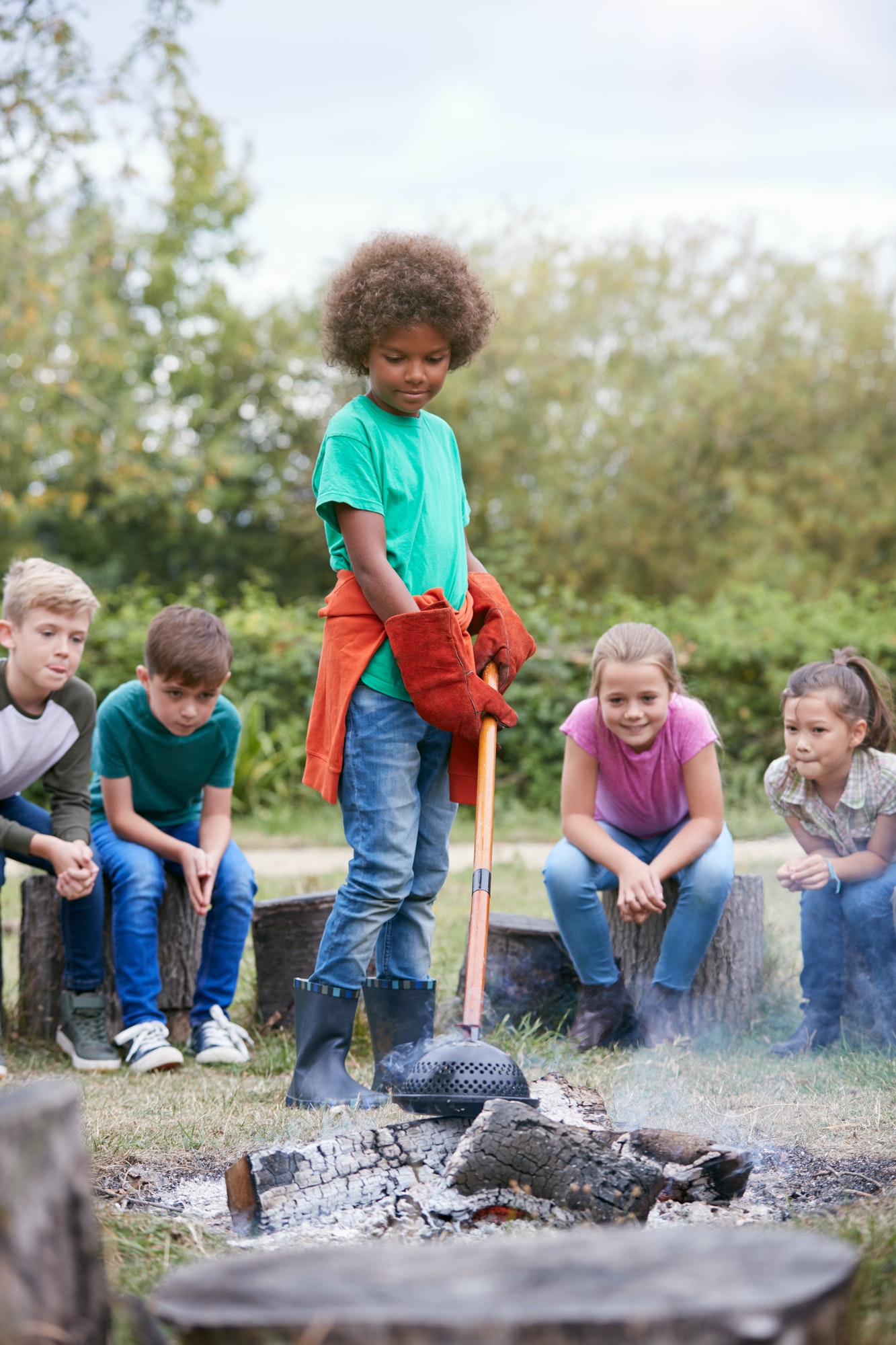 Group Of Children On Outdoor Activity Camping Trip Cooking Over Camp Fire Together